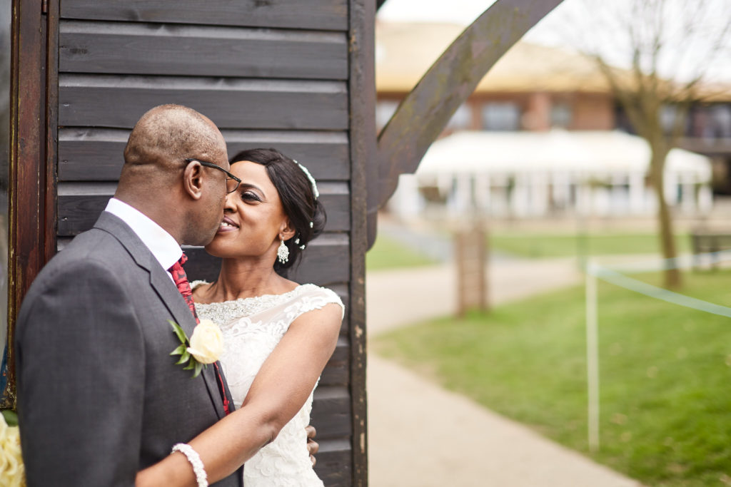 Bride and groom kissing beside a black timber building at Essex Golf Club