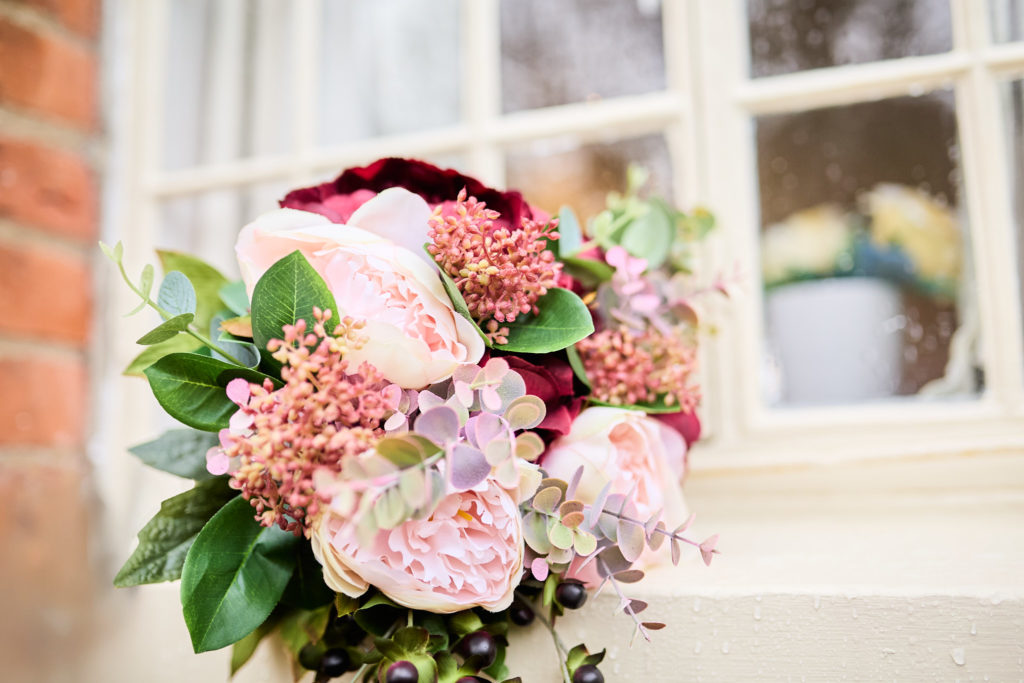 Bridal bouquet of pink, burgundy and cream flowers resting against a window
