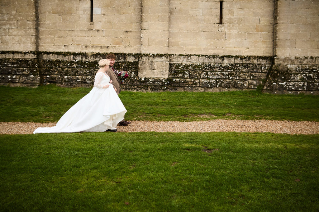 Bride walking across the lawn beneath the castle walls, her dress train behind her
