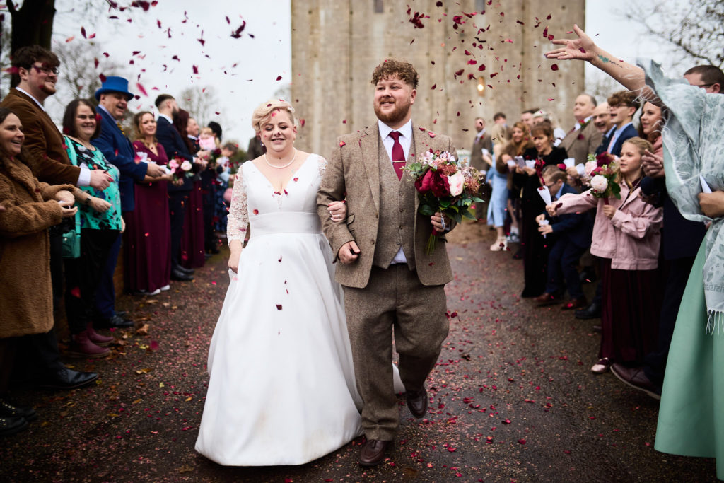 Bride and groom walking through confetti thrown by their guests at Hedingham Castle
