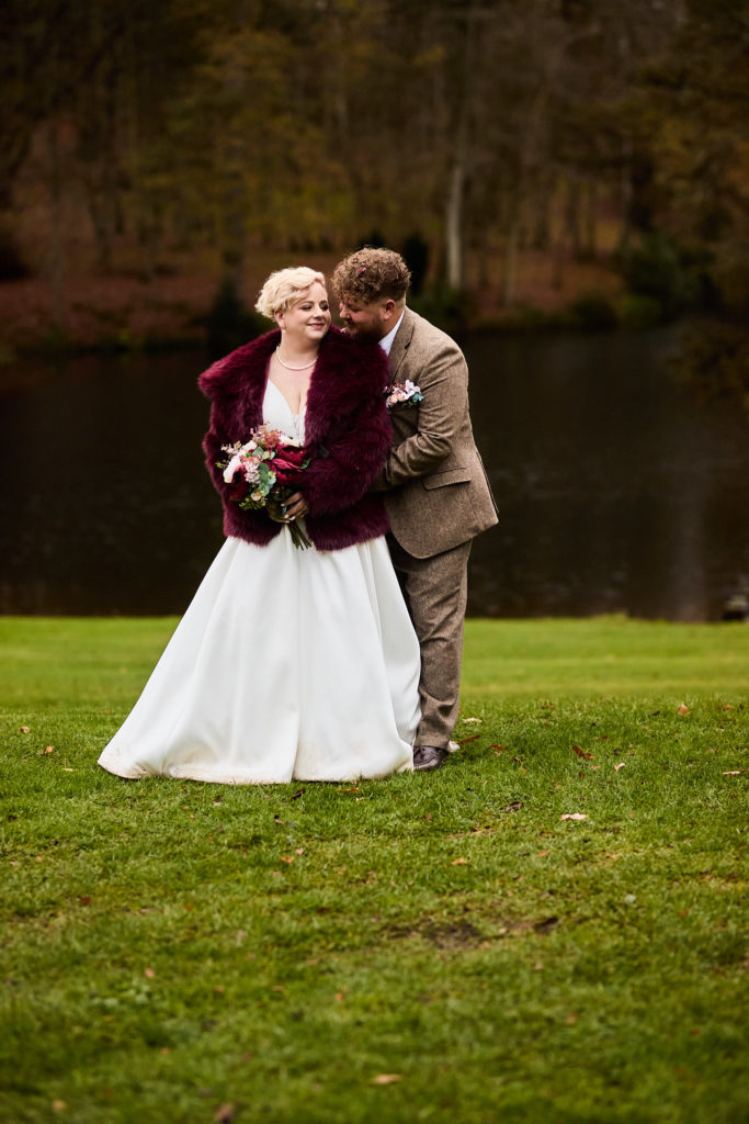 Groom kissing the bride's cheek beside the lake at Hedingham Castle
