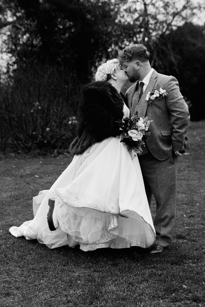 Black and white photo of the bride and groom kissing as her dress swishes, Hedingham Castle