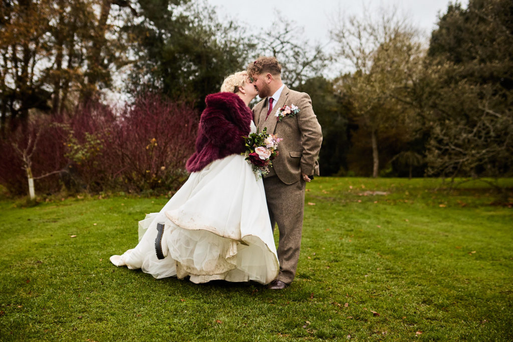 Bride and groom kissing on the lawn among autumn trees at Hedingham Castle