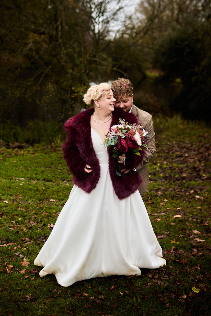 Bride laughing as the groom nuzzles her from behind in the grounds of Hedingham Castle