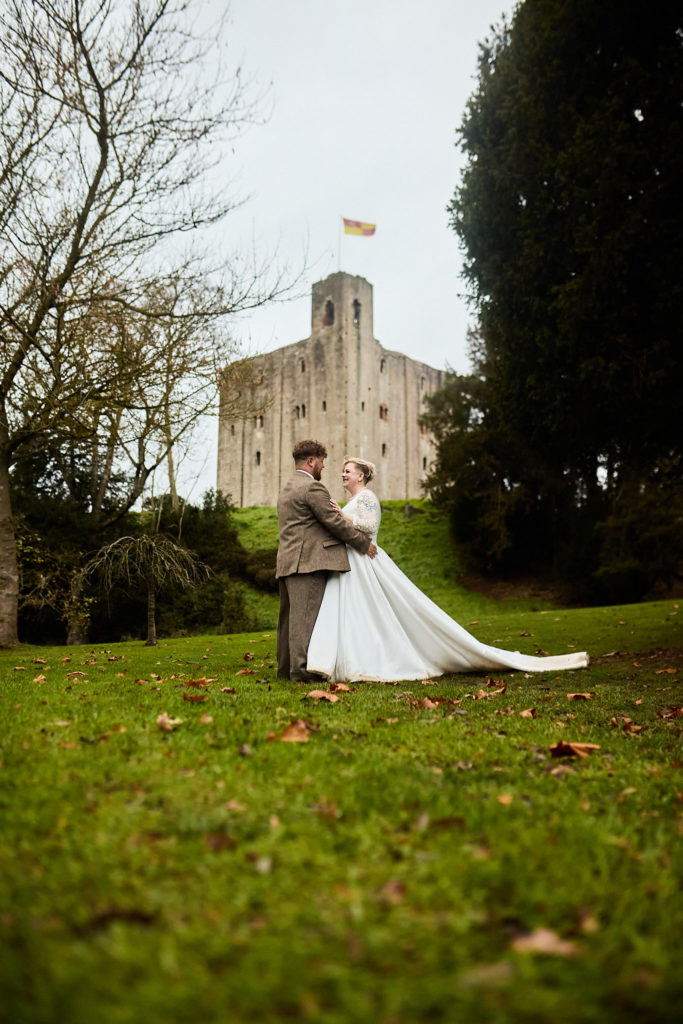Bride and groom with her dress train spread out in front of the keep at Hedingham Castle