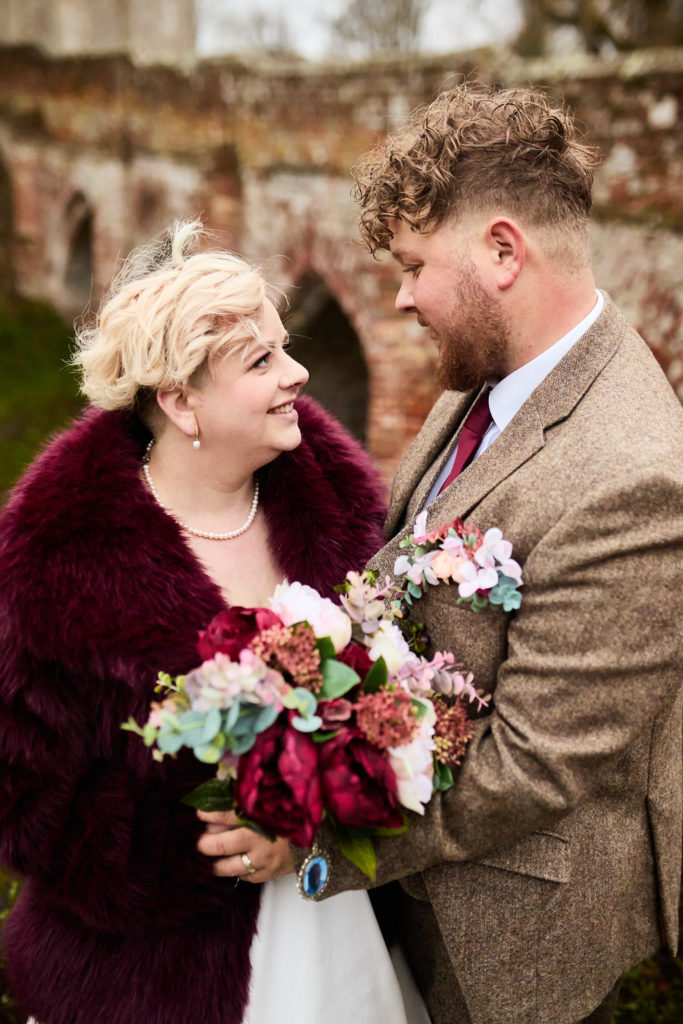 Bride and groom smiling at each other with her bouquet between them at Hedingham Castle, Essex