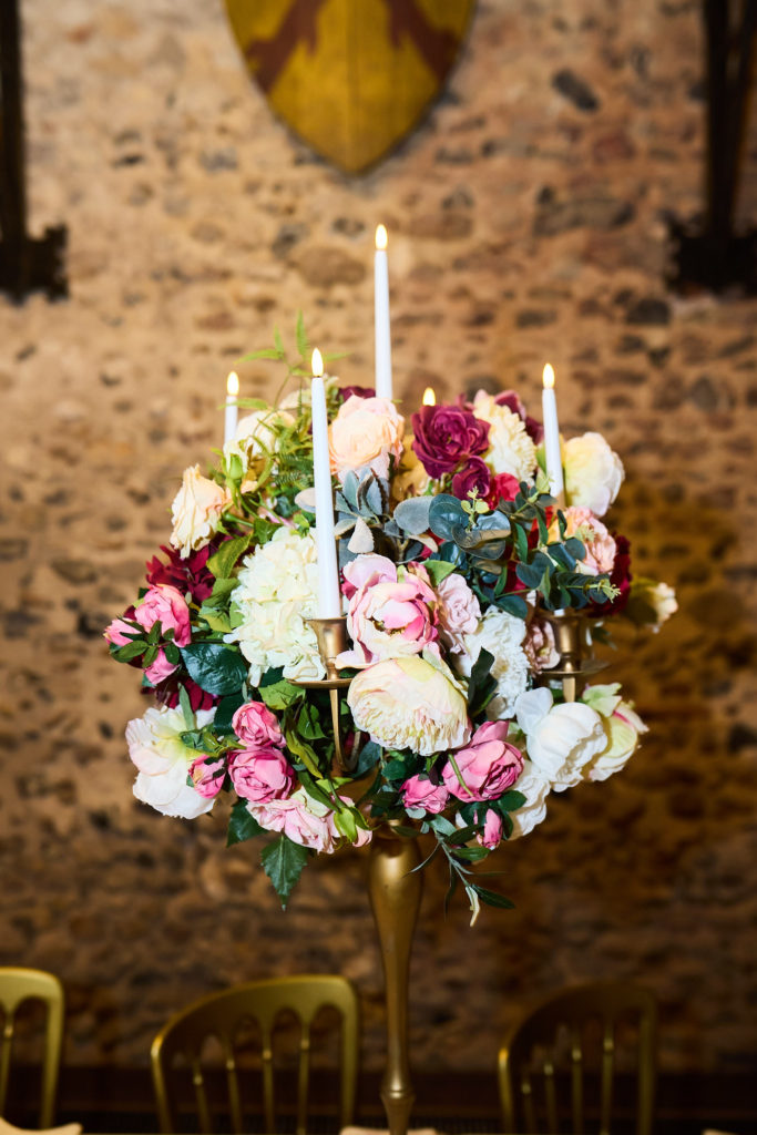 Tall candelabra centrepiece of pink, burgundy and cream flowers against a stone wall