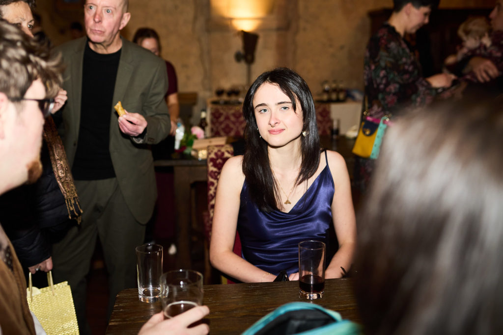 Wedding guest in a navy satin dress sitting with a drink