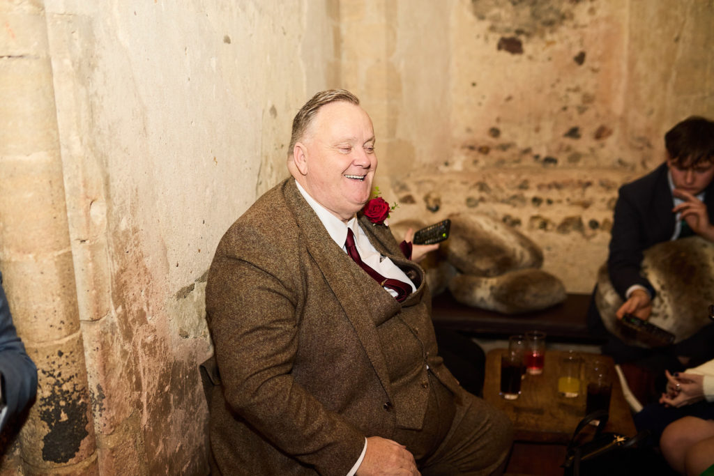 Older guest in a tweed suit smiling beside a stone wall