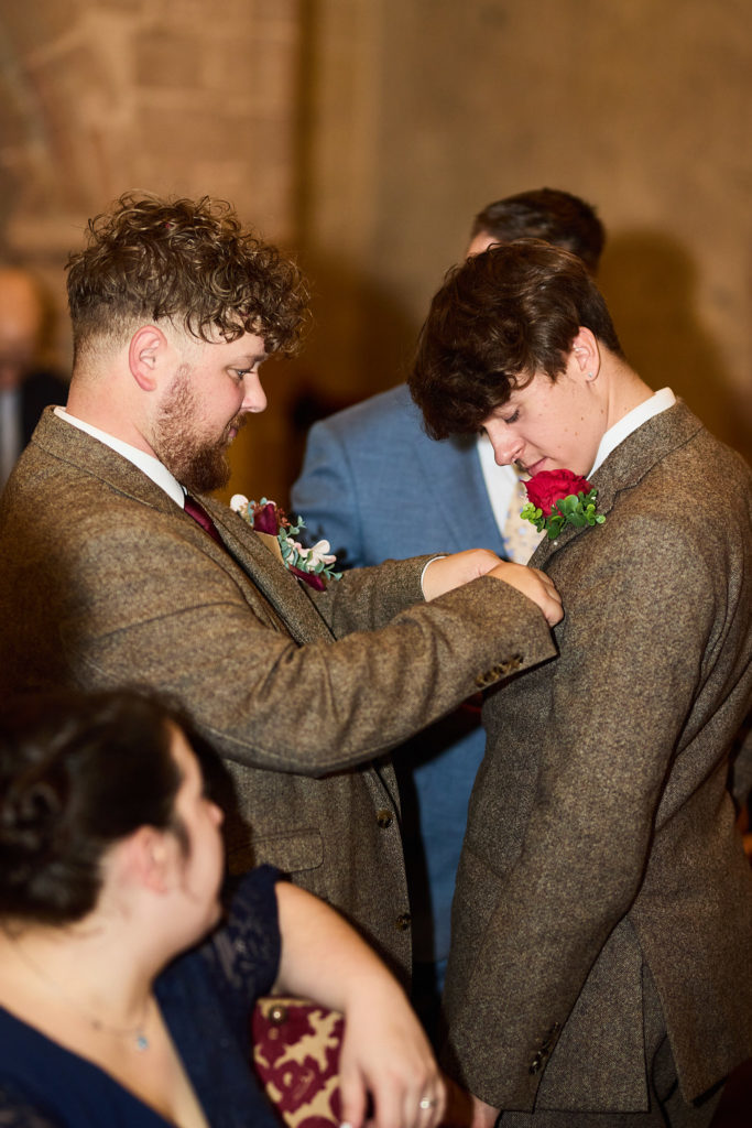 Groom pinning a buttonhole on a groomsman in a tweed suit