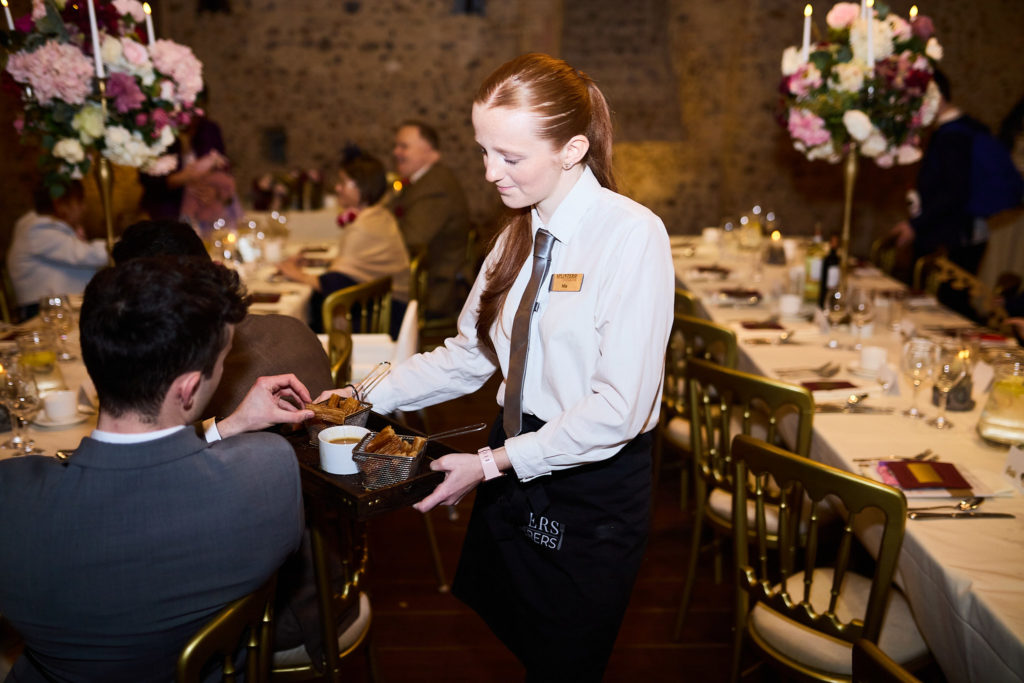 Waitress serving guests at the wedding breakfast in the castle hall