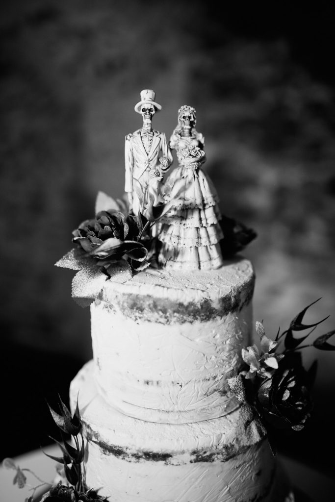 Black and white photo of a wedding cake topped with skeleton bride and groom figures