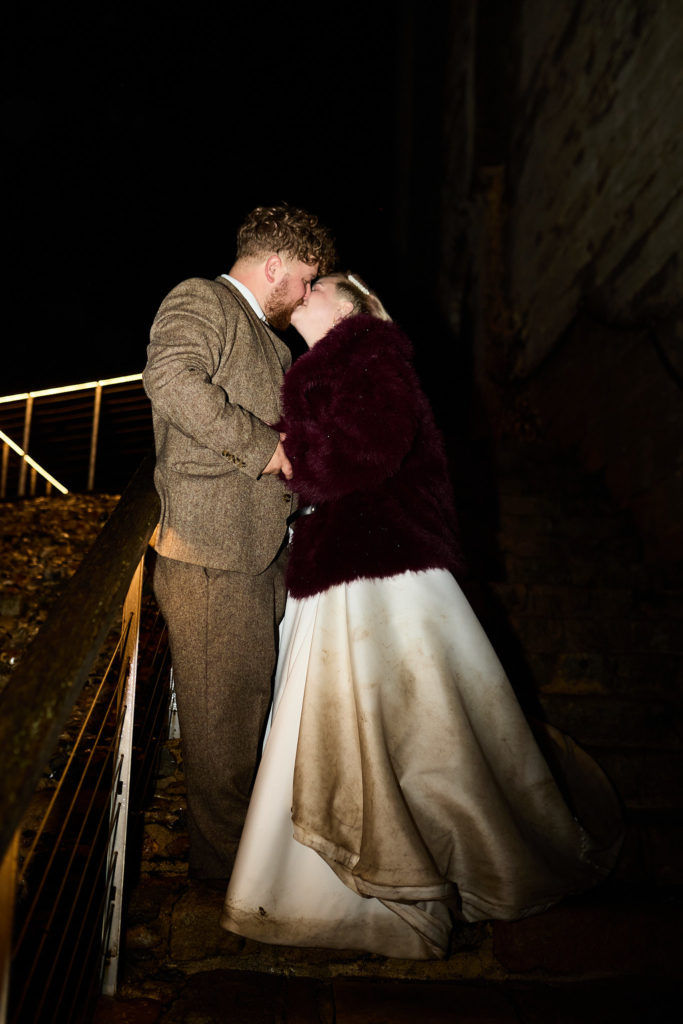 Bride and groom kissing on a gallery inside Hedingham Castle