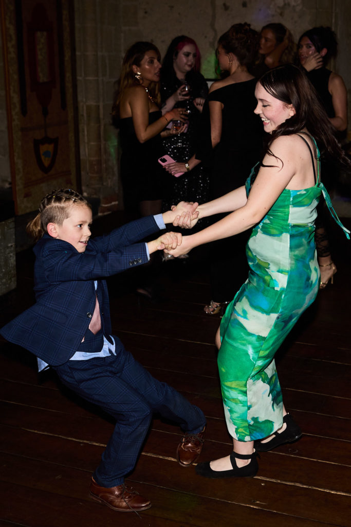 Boy in a navy suit swinging round with a woman in a green dress on the dance floor