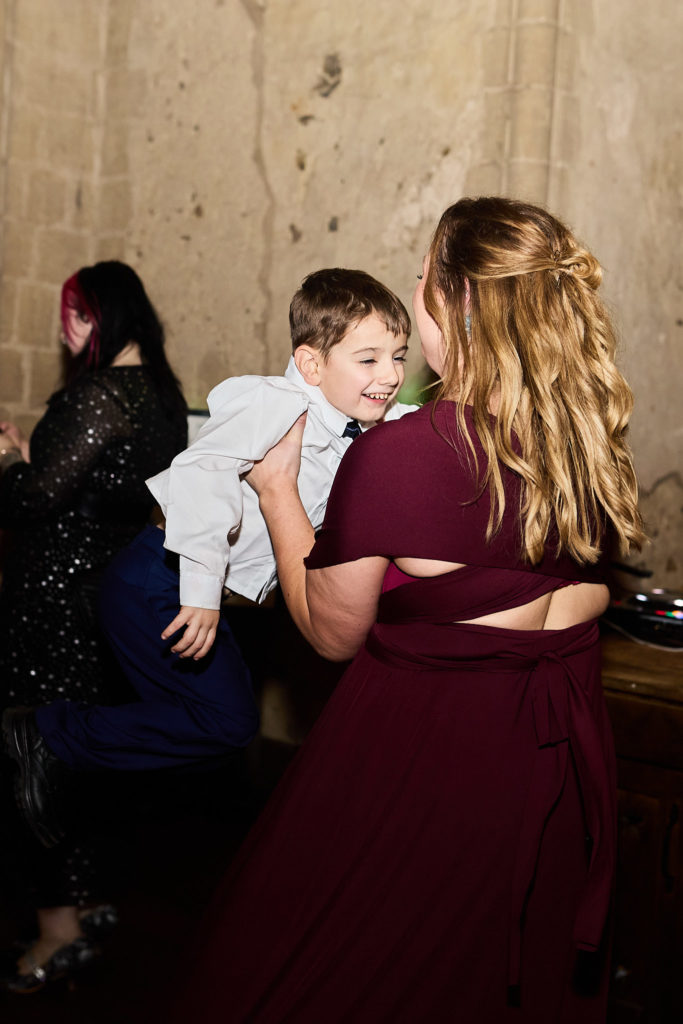 Bridesmaid in a burgundy dress lifting a laughing boy