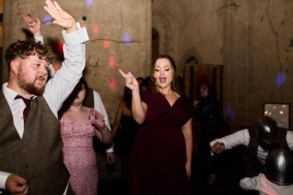 Groom dancing with his arm in the air among guests