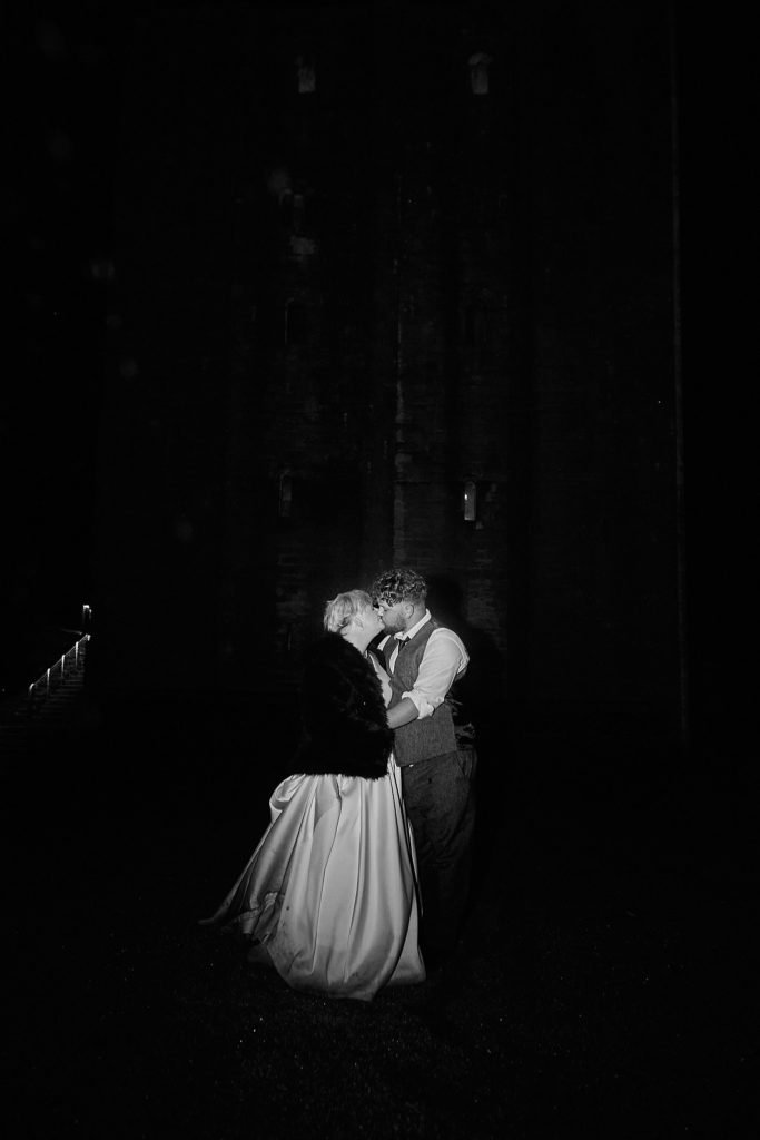 Black and white photo of the bride and groom kissing in a pool of light
