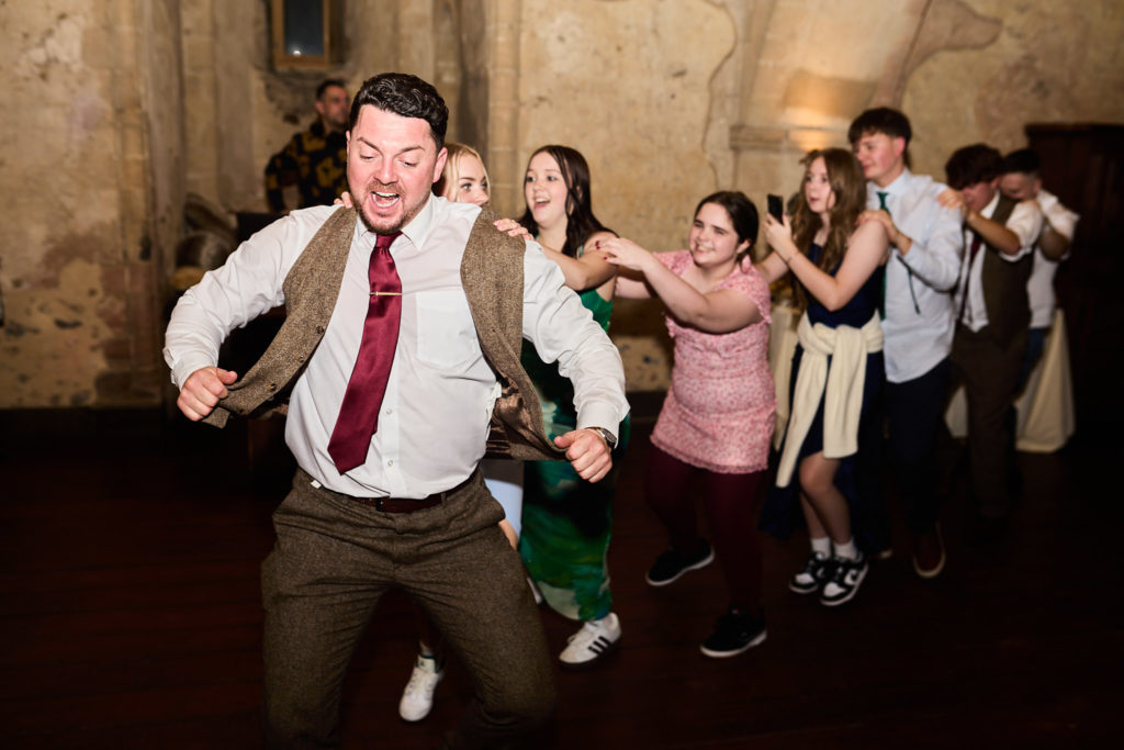 Man in a tweed waistcoat leading a line of dancing guests