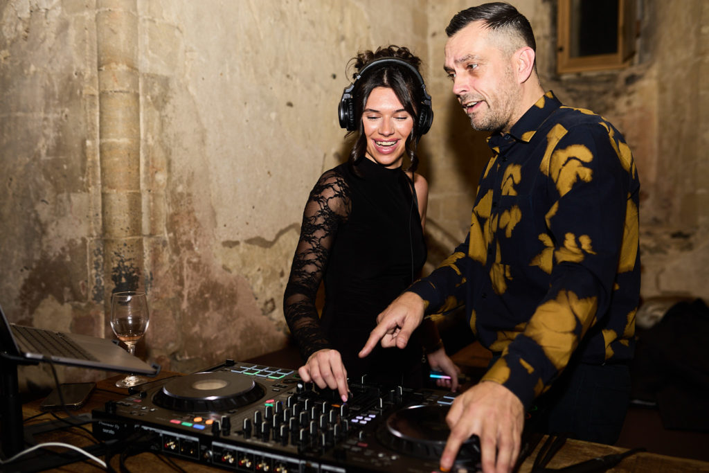 DJ at the decks with a guest beside him