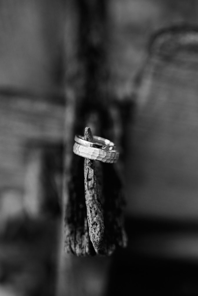 Black and white close-up of wedding rings balanced on a piece of bark
