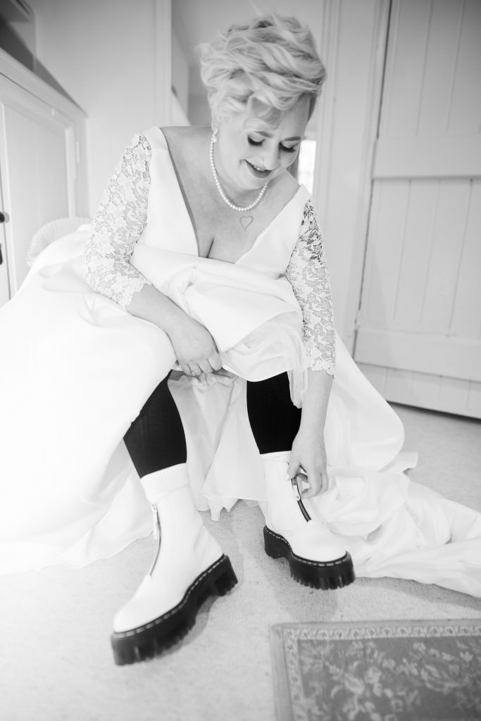 Black and white photo of the bride lacing up white Dr Martens boots under her wedding dress