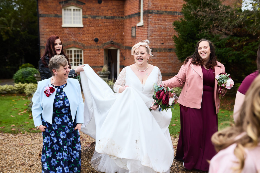 Bride walking with bridesmaids holding up her dress train outside the house at Hedingham Castle