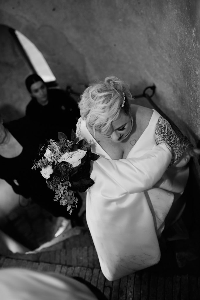 Black and white photo from above of the bride on the stairs with her bouquet