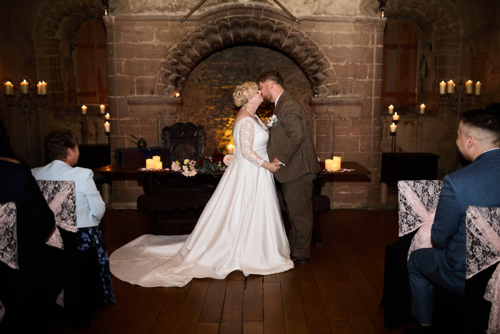 Bride and groom kissing beneath the stone arch at Hedingham Castle