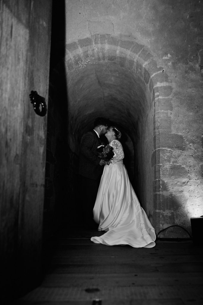 Black and white photo of the bride and groom kissing in a stone passageway at Hedingham Castle