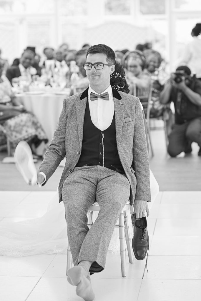 Black and white photo of the groom seated on the dance floor as guests watch