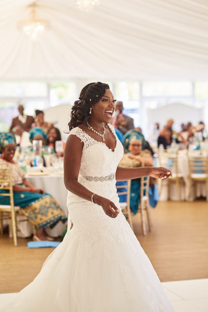 Bride laughing in her lace wedding dress as she walks across the dance floor at Quendon Hall