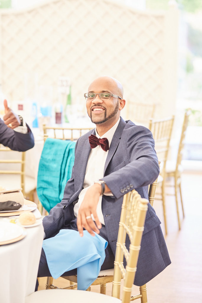 Wedding guest in a blue suit and burgundy bow tie smiling at the table