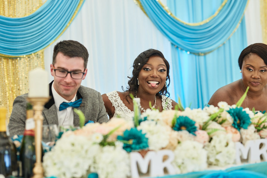Bride and groom smiling at the top table in front of blue and gold drapes