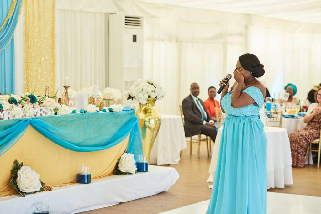 Bridesmaid in a turquoise dress facing the top table as she speaks