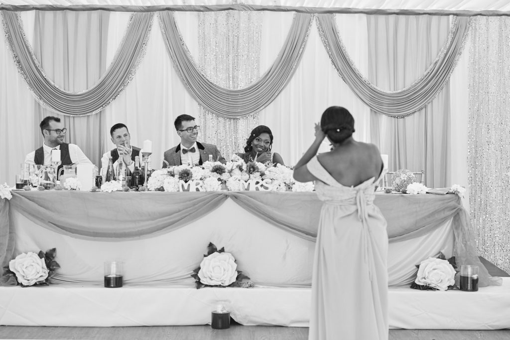 Black and white photo of a bridesmaid giving a speech in front of the top table
