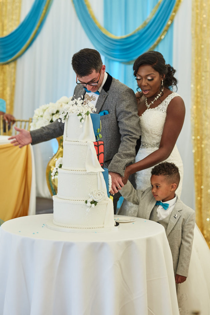 Bride and groom cutting their five-tier wedding cake with a young page boy