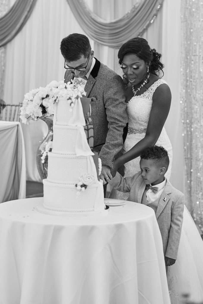 Black and white photo of the bride and groom cutting the cake with a page boy