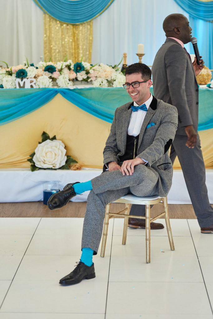 Groom laughing as he sits on a chair on the dance floor during a game