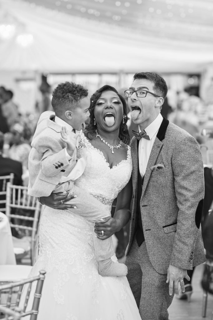 Black and white photo of the bride and groom sticking their tongues out with a page boy