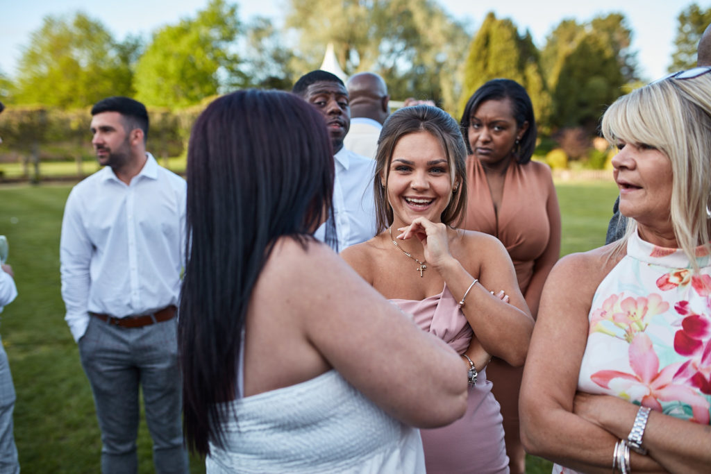 Wedding guests laughing together on the lawn at Quendon Hall