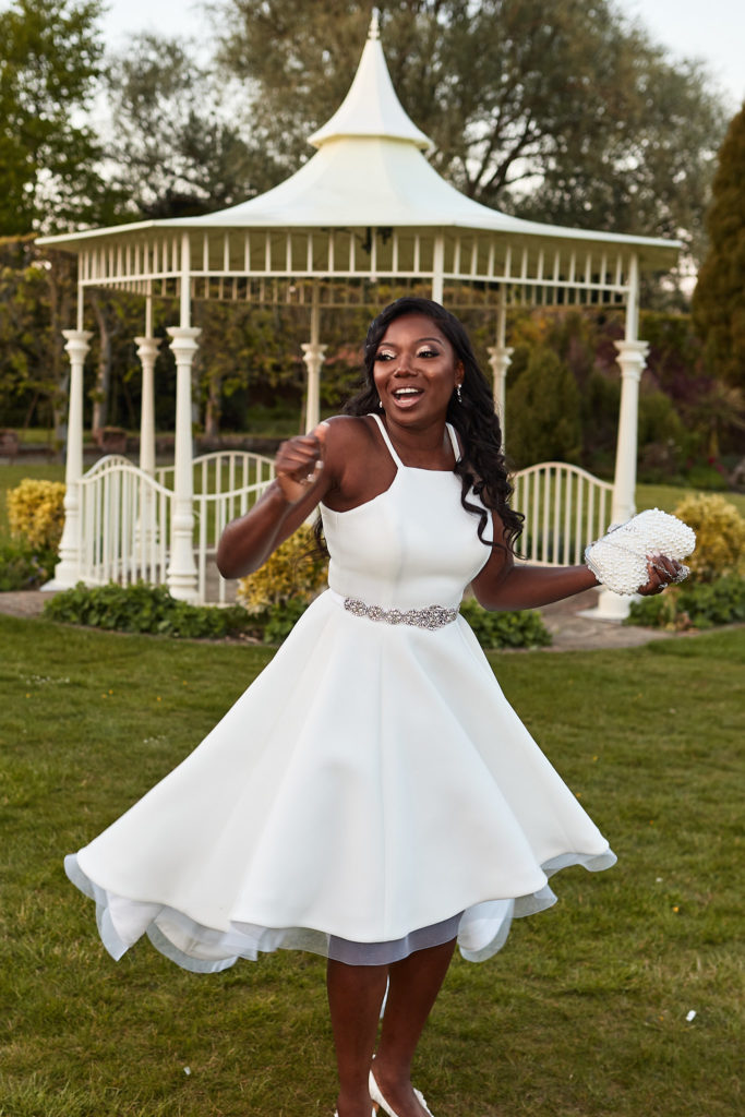 Bride twirling in a short white evening dress in front of the bandstand at Quendon Hall