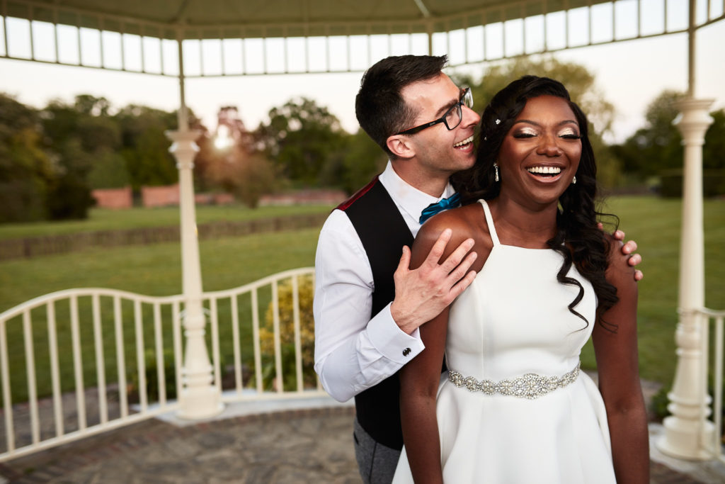 Groom kissing the bride's cheek in the bandstand at Quendon Hall as she laughs