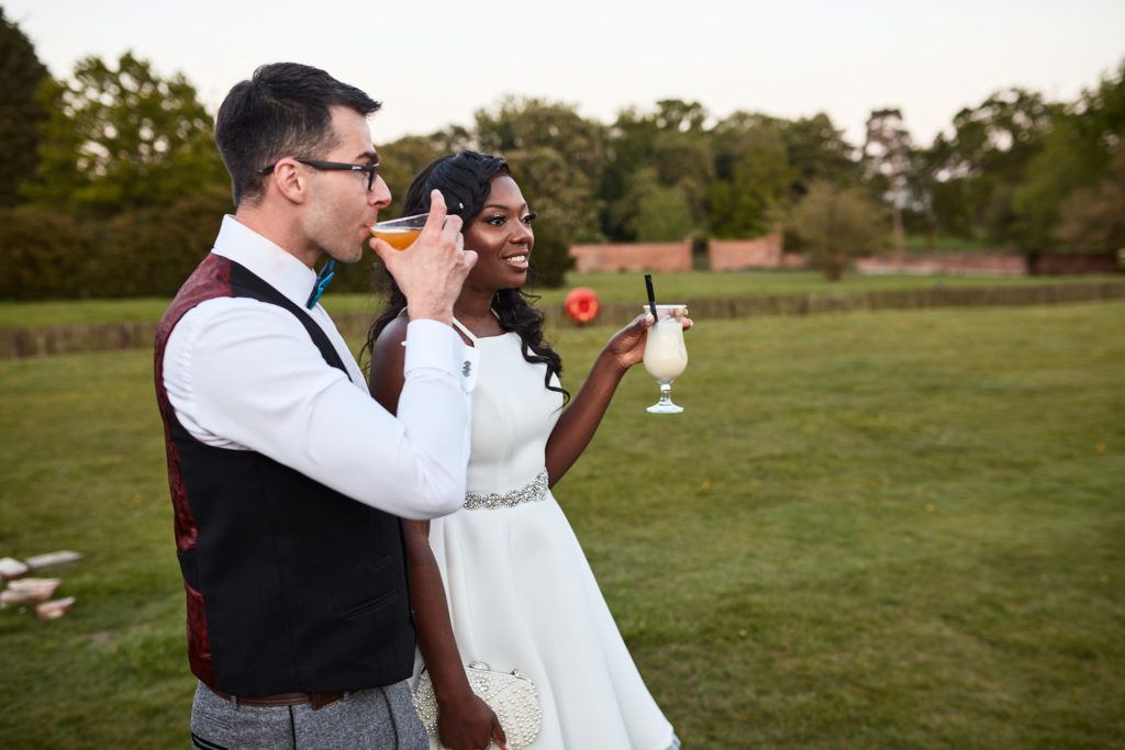 Bride and groom with drinks on the lawn at Quendon Hall at dusk