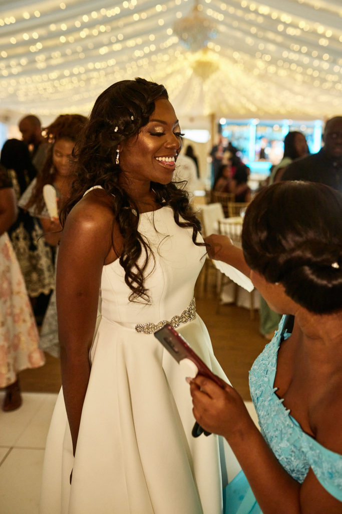 Bride in a white halterneck dress laughing with guests under fairy lights