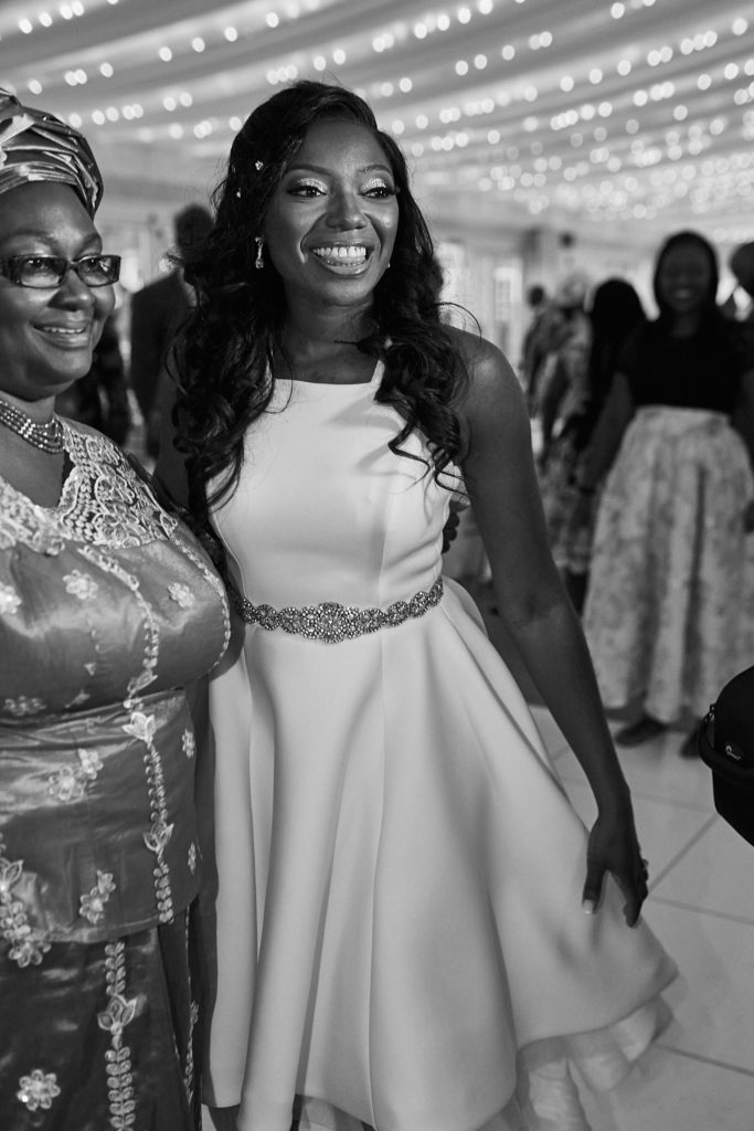 Black and white photo of the bride smiling beside a guest in a lace dress