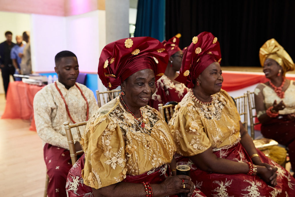 Women in red and gold traditional dress and head ties seated during the ceremony