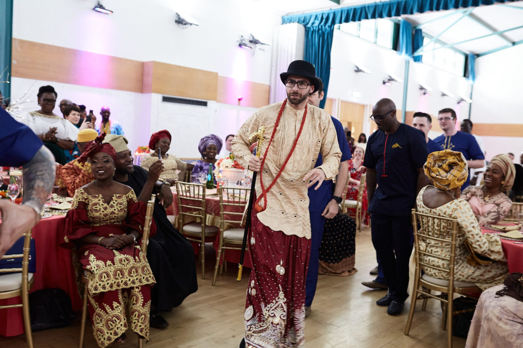 Groom walking through the hall in traditional dress as guests watch
