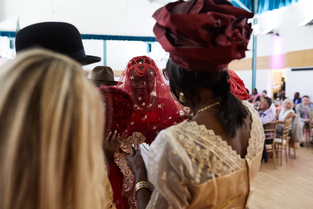 Guests watching the ceremony, seen from behind the groom's hat and a red head tie