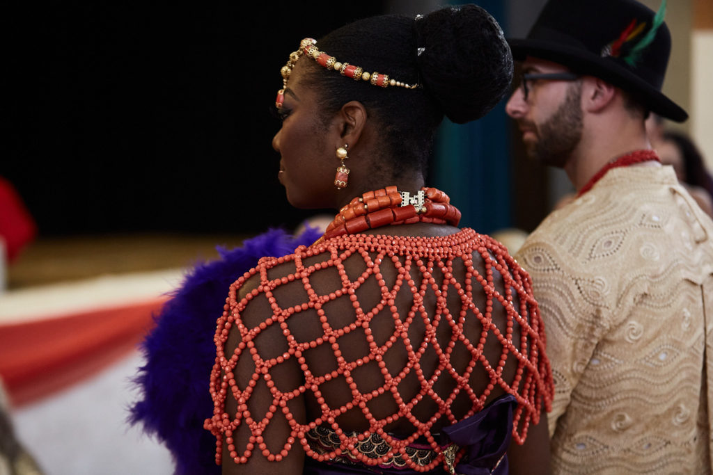 Bride in a coral bead cape seen from behind, facing the groom