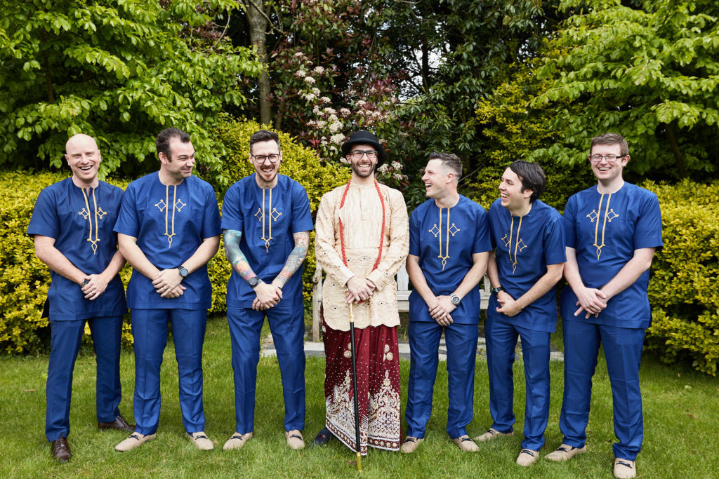 Groom in traditional dress lined up with his groomsmen in matching blue tunics
